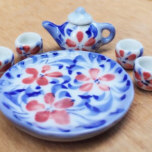 May include: A miniature tea set with a blue and white floral design. The set includes a teapot, four cups, and a plate.