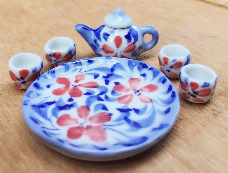 May include: A miniature tea set with a blue and white floral design. The set includes a teapot, four cups, and a plate.