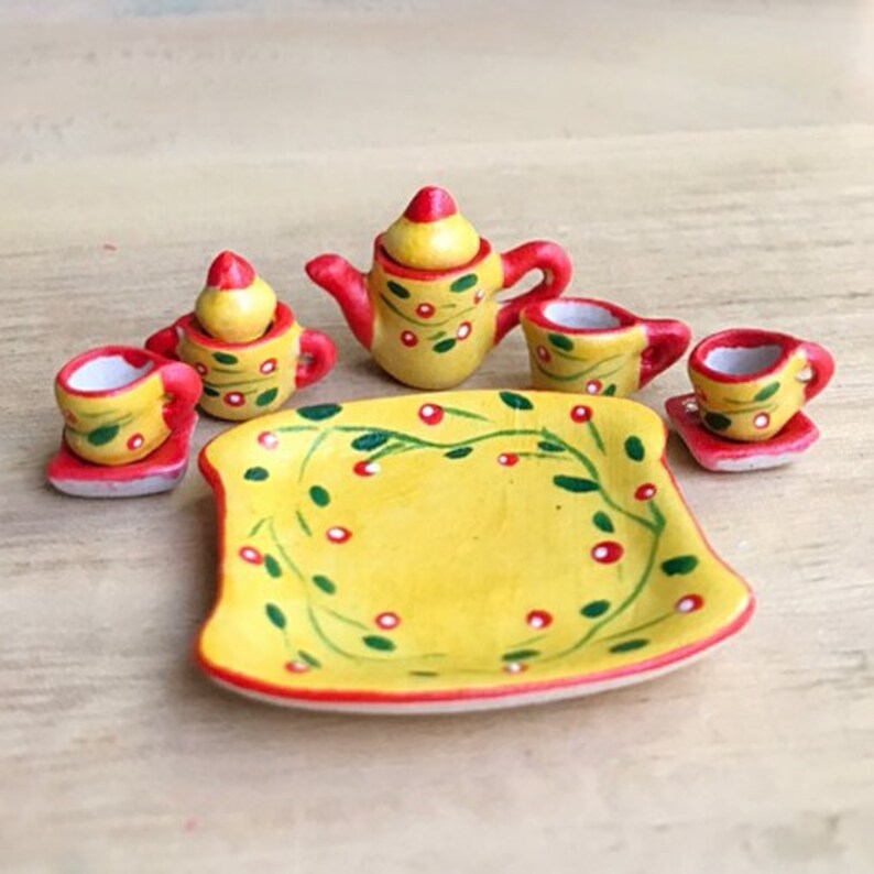 May include: A miniature yellow tea set with red and green floral designs. The set includes a teapot, creamer, sugar bowl, four cups, and a matching serving tray.