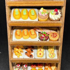 May include: A miniature wooden bakery display filled with various pastries. The shelves hold cakes, tarts, croissants, and other baked goods, all intricately detailed with colorful frosting and toppings. A charming, detailed food display.