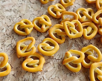 May include: A close-up of a group of small, golden brown pretzels on a cork surface. The pretzels are arranged in a random pattern, with some overlapping.