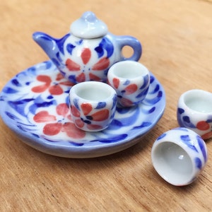 May include: A miniature tea set with a blue and white floral design. The set includes a teapot, four cups, and a matching saucer.
