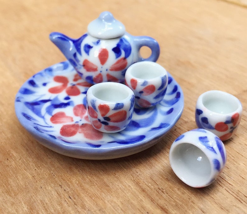 May include: A miniature tea set with a blue and white floral design. The set includes a teapot, four cups, and a matching saucer.