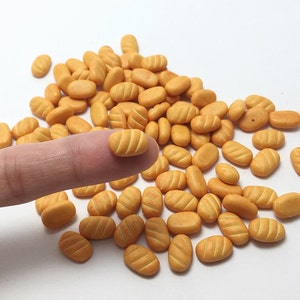 Puede incluir: Un montón grande de panecillos miniatura de color marrón claro. Los panecillos están hechos de arcilla polimérica y tienen aproximadamente el tamaño de una uña.