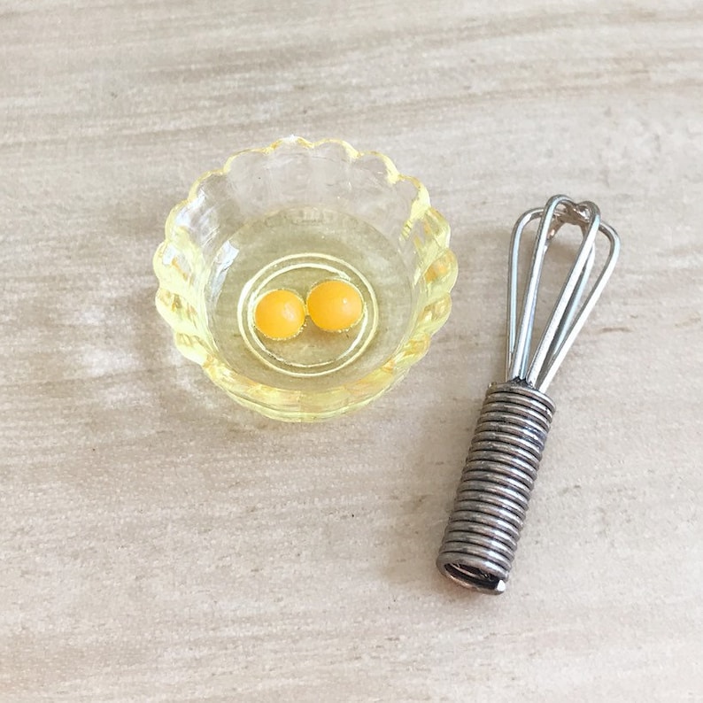 Peut inclure: Un petit bol en verre jaune &agrave; bord festonn&eacute; contenant deux jaunes d'&oelig;ufs jaune vif, &agrave; c&ocirc;t&eacute; d'un mini fouet argent&eacute; avec une poign&eacute;e en spirale. Les articles sont dispos&eacute;s sur une surface claire.