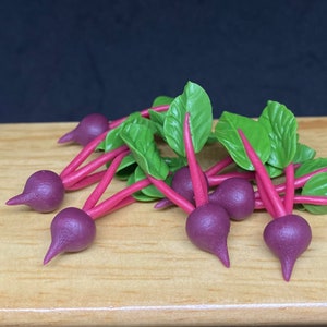 May include: A group of miniature beet root vegetables with green leaves, arranged on a wooden surface. The beets are a deep purple color and the leaves are a bright green.