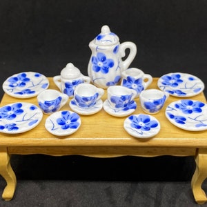 May include: Miniature porcelain tea set with blue floral patterns. The set includes a teapot, creamer, sugar bowl, cups, saucers, and plates. The tea set is displayed on a small wooden table.