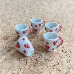 May include: Five white ceramic teacups with red heart and dot patterns. The cups have a small handle on the side.