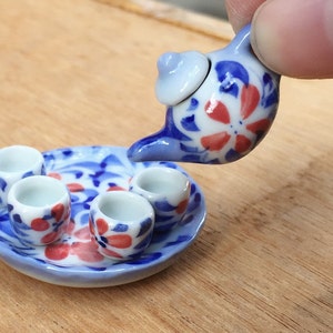 May include: A miniature tea set with a blue and white floral design. The set includes a teapot, four cups, and a saucer.