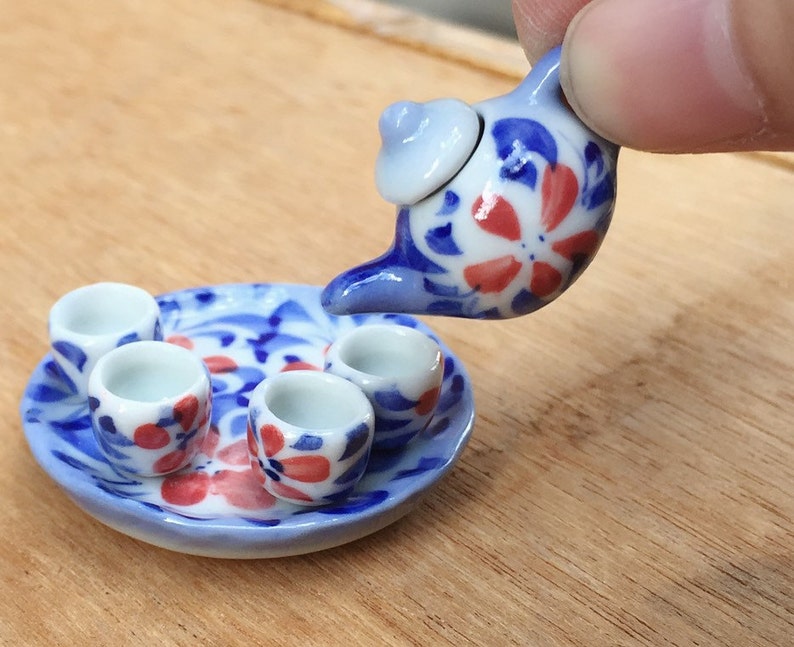 May include: A miniature tea set with a blue and white floral design. The set includes a teapot, four cups, and a saucer.