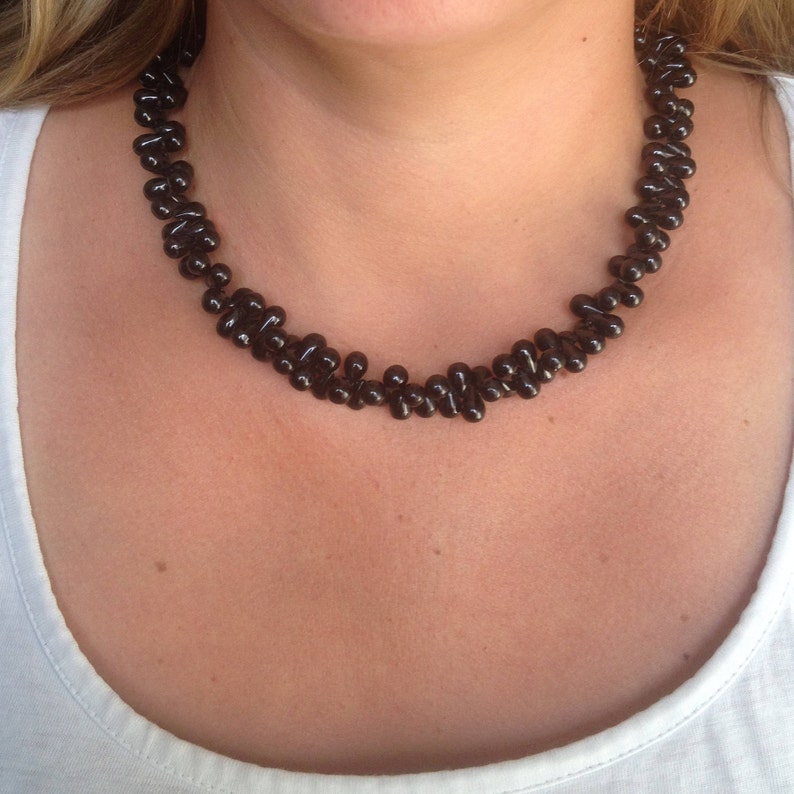 May include: A dark brown beaded necklace. The necklace is made of small, rounded beads strung together in a close pattern. The beads have a glossy finish and are arranged to sit around the neck.