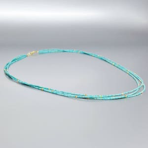Peut inclure: Un collier superposé turquoise et or avec de petites perles. Le collier est composé de plusieurs rangs de perles turquoise avec de petites perles dorées réparties sur toute la longueur.