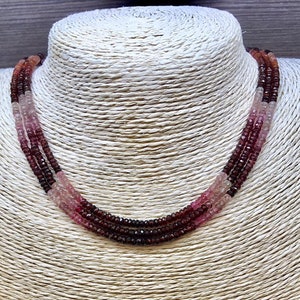 May include: A three-strand necklace made of pink, red, and dark red gemstone beads.