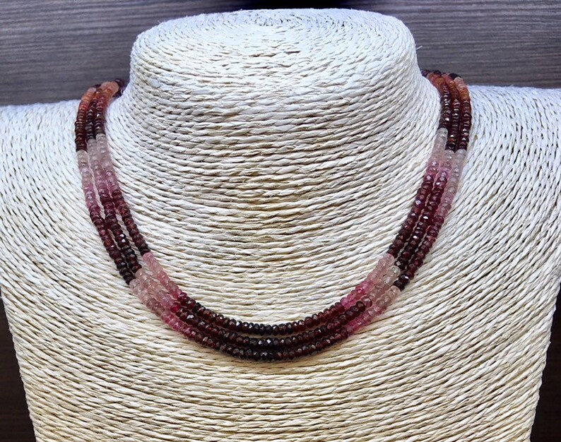 May include: A three-strand necklace made of pink, red, and dark red gemstone beads.