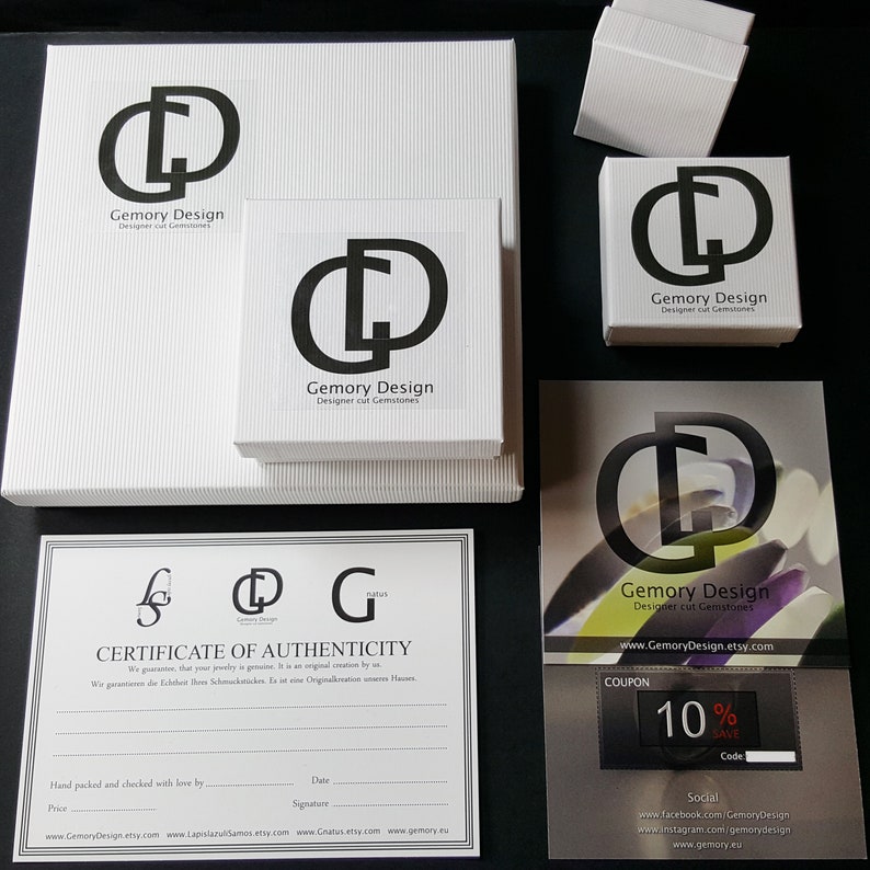 May include: A white box with the logo "Gemory Design" and the text "Designer cut Gemstones". The box is sitting on a white surface. There is a certificate of authenticity with the text "Gemory Design" and "Certificate of Authenticity". There is also a coupon with the text "Gemory Design" and "10% SAVE".