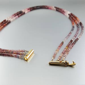 May include: A multi-strand necklace made of pink, red, and clear faceted gemstone beads. The necklace has a gold clasp and is approximately 18 inches long.