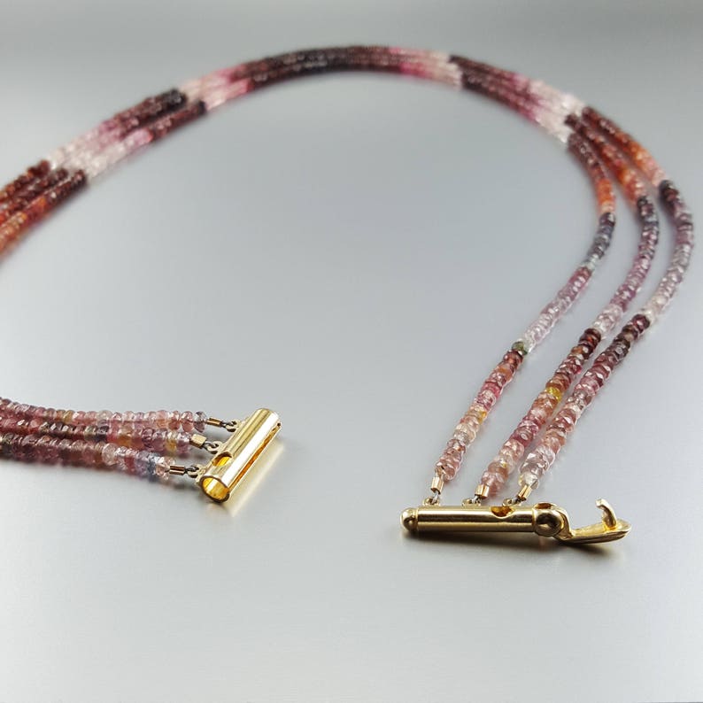 May include: A multi-strand necklace made of pink, red, and clear faceted gemstone beads. The necklace has a gold clasp and is approximately 18 inches long.