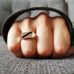 Op de afbeelding: Een gouden ring met een zwarte diagonale streep over de bovenkant.