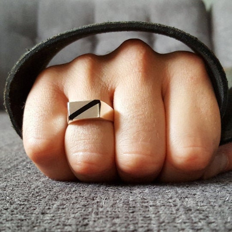 Op de afbeelding: Een gouden ring met een zwarte diagonale streep over de bovenkant.
