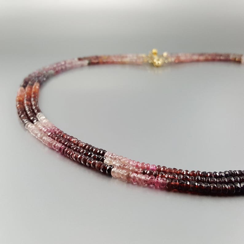May include: A multi-strand necklace made of pink and red gemstone beads. The beads are faceted and have a graduated size, with the largest beads at the bottom of the necklace.