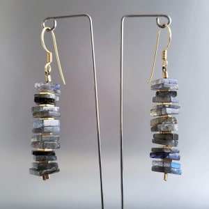 May include: A pair of gold dangle earrings with a stack of labradorite stones. The stones are a mix of gray, black, and blue.