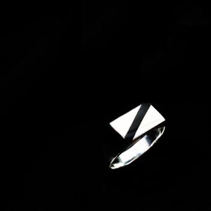 Op de afbeelding: Een zilveren ring met een rechthoekige zwarte en witte steen.