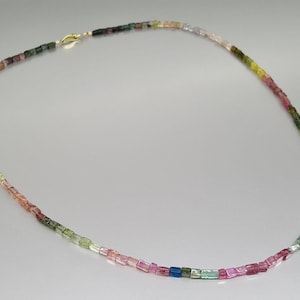 May include: A multi-colored gemstone necklace with square-shaped beads in shades of pink, green, blue, and yellow. The necklace is made of natural gemstones and has a gold clasp.