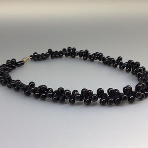 May include: A black beaded necklace with a silver clasp. The necklace is made of small, round, glossy black beads arranged in a clustered pattern. The beads are strung together to form a curved shape.
