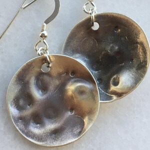 May include: A pair of silver earrings with a hammered, textured, circular design. The earrings have a simple hook closure.