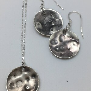 May include: A silver necklace and earrings set with textured round pendants. The pendants have a hammered, organic look.