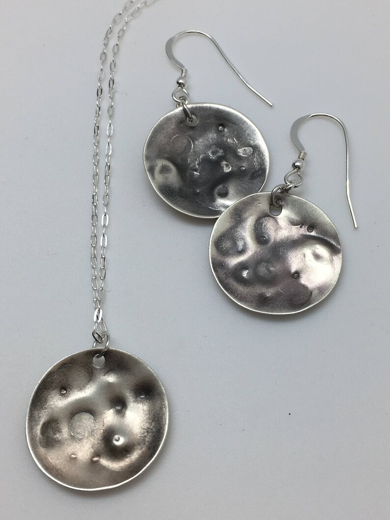 May include: A silver necklace and earrings set with textured round pendants. The pendants have a hammered, organic look.