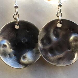 May include: A pair of silver earrings with a textured, hammered finish. The earrings are round and have a slightly irregular shape.