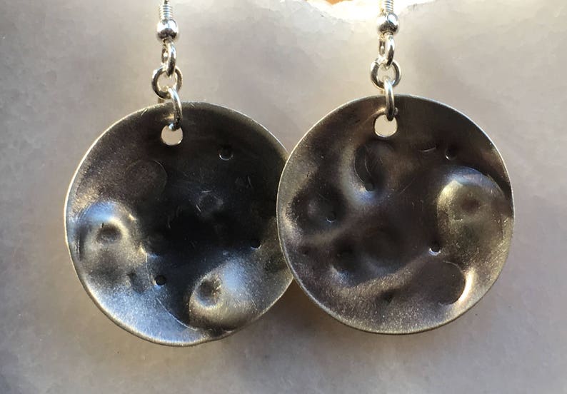 May include: A pair of silver earrings with a textured, hammered finish. The earrings are round and have a slightly irregular shape.