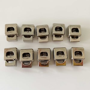 May include: Ten silver-toned metal clasps with a spring mechanism. The clasps are square-shaped and have a small hole in the centre.