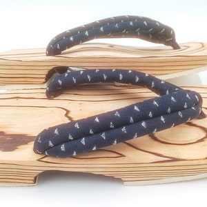 May include: A pair of wooden geta sandals with a blue and white patterned strap. The sandals are made of natural wood and have a traditional Japanese design.