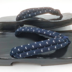 May include: A pair of black geta sandals with a blue and white patterned fabric strap. The sandals have a wooden base and a raised platform.