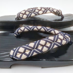 May include: A pair of black wooden geta sandals with a white and blue geometric patterned fabric strap.