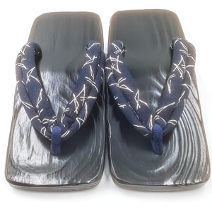 May include: A pair of black wooden geta sandals with navy blue and white patterned straps. The straps are tied in a knot at the front of the sandals.