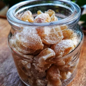Puede incluir: Un tarro de vidrio lleno de caramelos de jengibre azucarados. Los caramelos son de color marrón claro y están cubiertos de azúcar blanco.