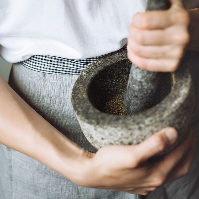 May include: A person grinding spices in a gray stone mortar and pestle.