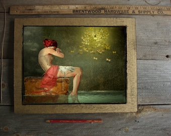 May include: A woman in a red dress and corset sits on a vintage suitcase with her head in her hands.  She is surrounded by a swarm of golden butterflies.  The scene is lit by a single lightbulb hanging from the ceiling.