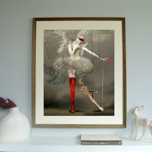 May include: A framed digital art print featuring a winged figure in a white ruffled dress, wearing a red blindfold and one red boot. The figure is suspended by thin gold chains, with a small red sphere floating near the outstretched hand.