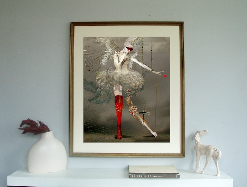 May include: A framed digital art print featuring a winged figure in a white ruffled dress, wearing a red blindfold and one red boot. The figure is suspended by thin gold chains, with a small red sphere floating near the outstretched hand.