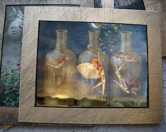 May include: A framed artwork featuring three glass bottles with a whimsical fairy scene inside each. The bottles are filled with a swirling, ethereal mist and each fairy is depicted with delicate wings and flowing hair. The artwork is set against a dark blue background with a crescent moon and stars.