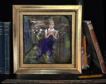 May include: A framed artwork depicts a fairy with butterfly wings reading a book, set against a backdrop of a path and buildings. The frame is gold. Books and pencils are on a shelf. A ruler is at the bottom.