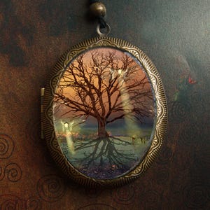 May include: A bronze locket necklace with a glass cameo featuring a detailed image of a bare tree with a light brown trunk and branches against a background of a hazy, golden sunset.