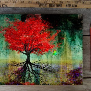 May include: A vibrant art print featuring a tree with bright red leaves and exposed roots. The background blends teal, green, and yellow hues. A red pencil rests on a wooden surface, alongside a vintage measuring stick.