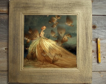 May include: A framed artwork featuring a woman in a golden gown with butterfly-like wings. The artwork has a vintage aesthetic, with a gold-colored frame. A yellow pencil rests on the wooden surface.