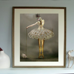May include: A framed art print featuring a surreal, mixed media image of a woman in a white tutu and a top hat, holding a chain attached to a small, white, animal-like figure. The background is a muted gray.