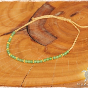 May include: A green gemstone beaded necklace with gold accents on a natural wood background. The necklace is made with a simple string and has a sliding knot for adjusting the length.